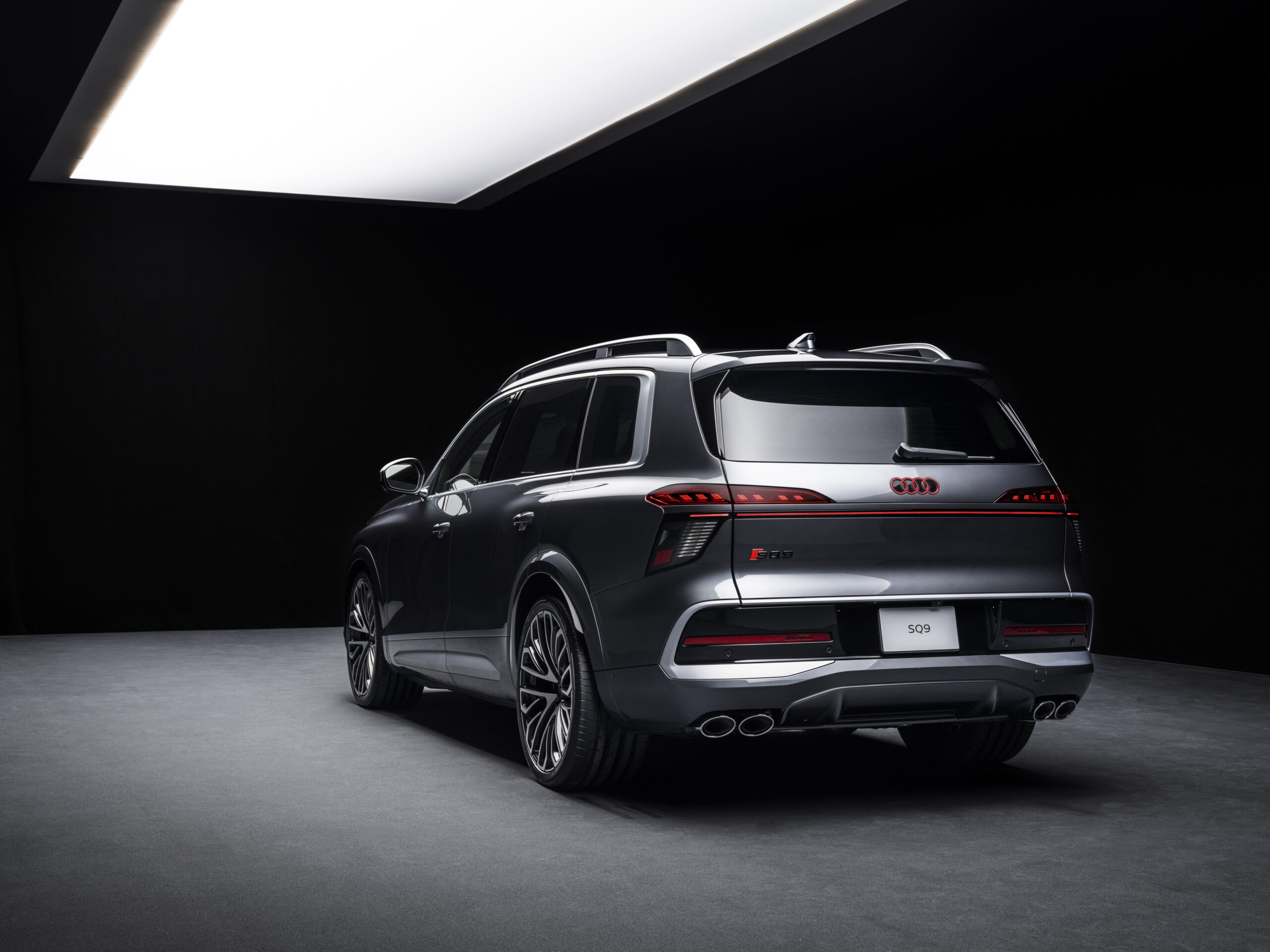Tumehall Audi SQ9 tagumine külgvaade stuudiovalguses koos valgustatud Audi logo ja SQ9 tähisega