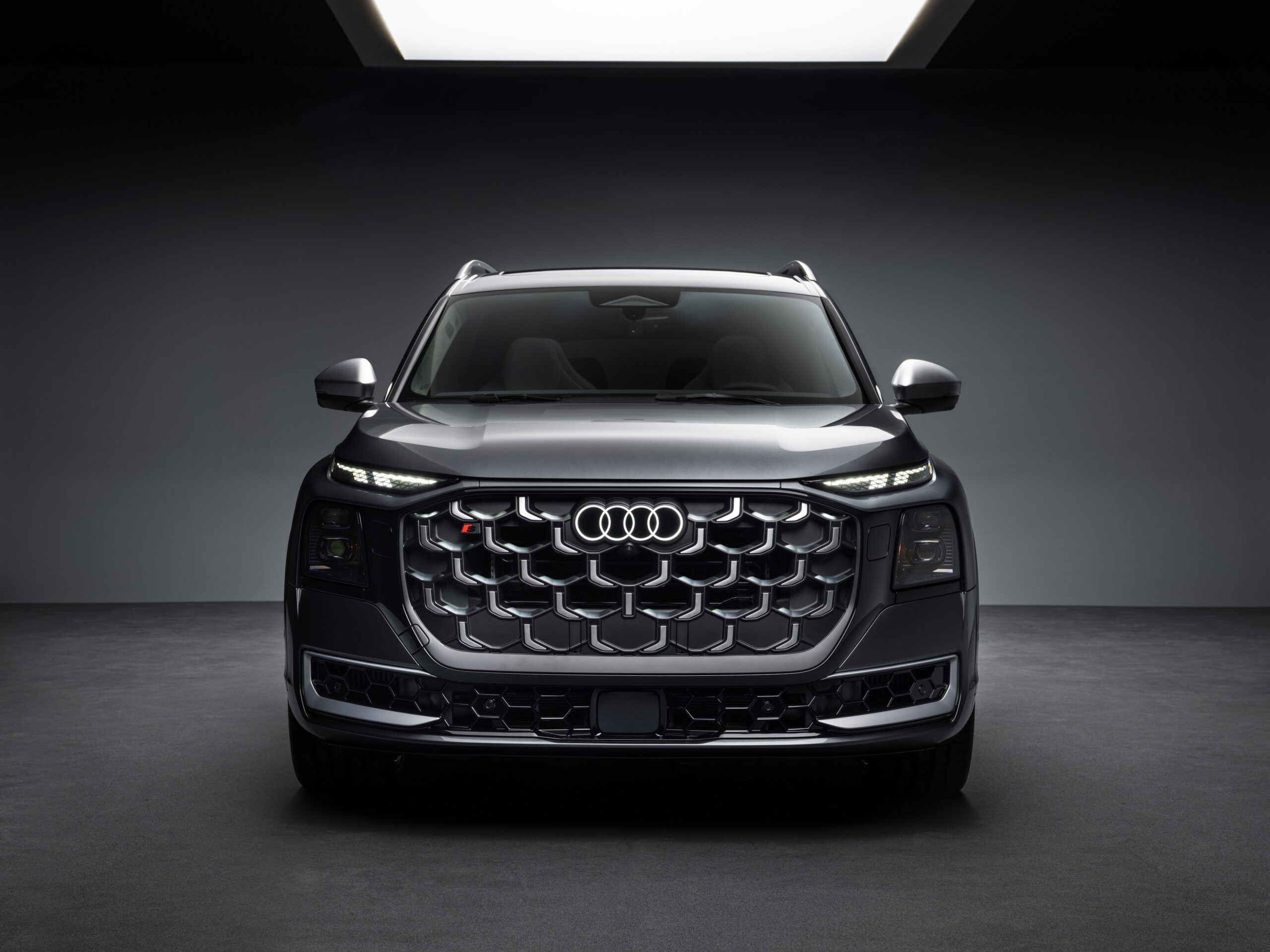 Audi SQ9 esiosa otsevaates stuudiovalguses koos valgustatud Audi logoga