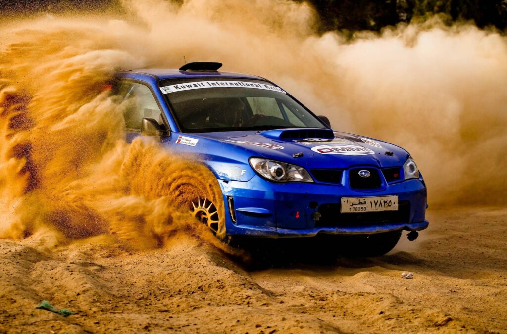 Sinine Subaru Impreza ralliauto tolmupilves Sinine Subaru Impreza ralliauto läbimas liivast kurvi Kuwait International Rally võistlusel