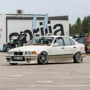 Valge madaldatud kahetoonilise kerekomplektiga BMW E36 sedaan driftiauto sõitmas Porsche Ringi boksiteel Augustfest 2026 festivalil