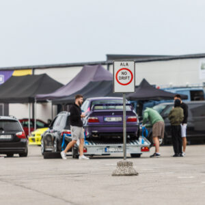 Liiklusmärk ALA NO DRIFT Porsche Ringi boksiteel ja taustal treileril olev lilla BMW E36 driftiauto Augustfest 2026 festivalil