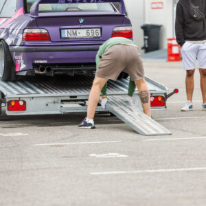 Mees paigaldamas kaldteed autotrepilerile lilla BMW E36 driftiauto mahalaadimiseks Porsche Ringi paddock-alal Augustfest 2026 festivalil