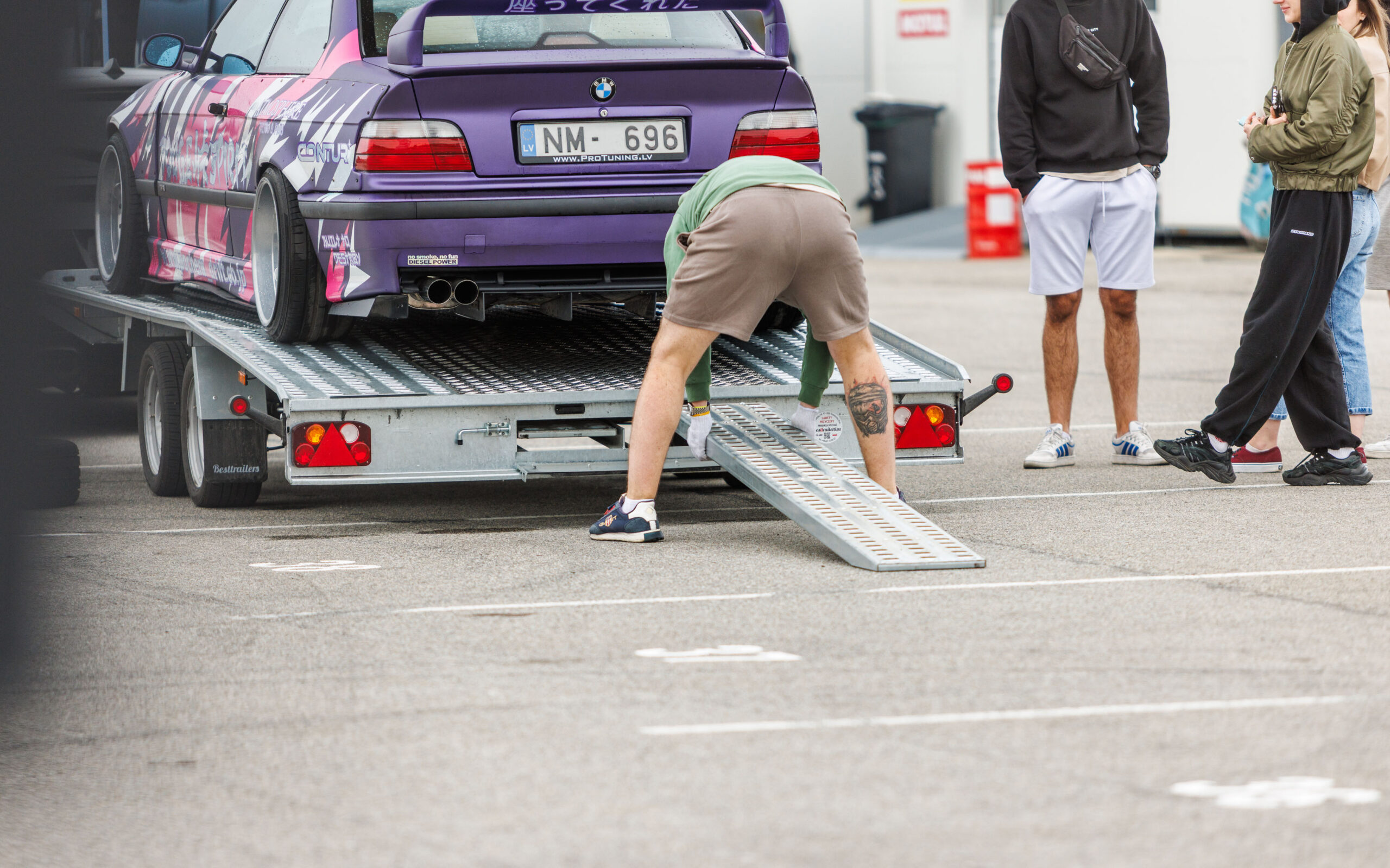 Mees paigaldamas kaldteed autotrepilerile lilla BMW E36 driftiauto mahalaadimiseks Porsche Ringi paddock-alal Augustfest 2026 festivalil