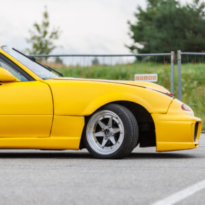 Kollane madaldatud Mazda MX-5 NA sportauto laiendatud poritiibade ja poleeritud randiga retrovelgedega Porsche Ringi asfaltplatsil Augustfest 2026 festivalil