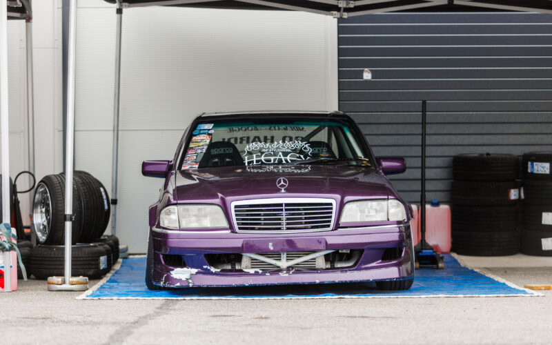 Lilla Mercedes-Benz C-klassi W202 driftiauto suure vahejahuti ja Sparco istmetega hooldustelgi all Porsche Ringi boksiteel Augustfest 2026 festivalil