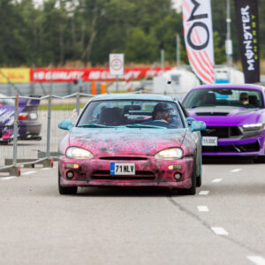 Kirju custom-värviga Mazda MX-3 sportkupee sõitmas Porsche Ringi rajal lilla Ford Mustang S650 ees Augustfest 2026 festivalil