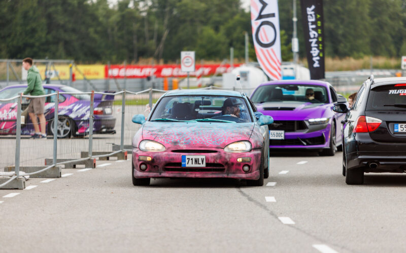Kirju custom-värviga Mazda MX-3 sportkupee sõitmas Porsche Ringi rajal lilla Ford Mustang S650 ees Augustfest 2026 festivalil