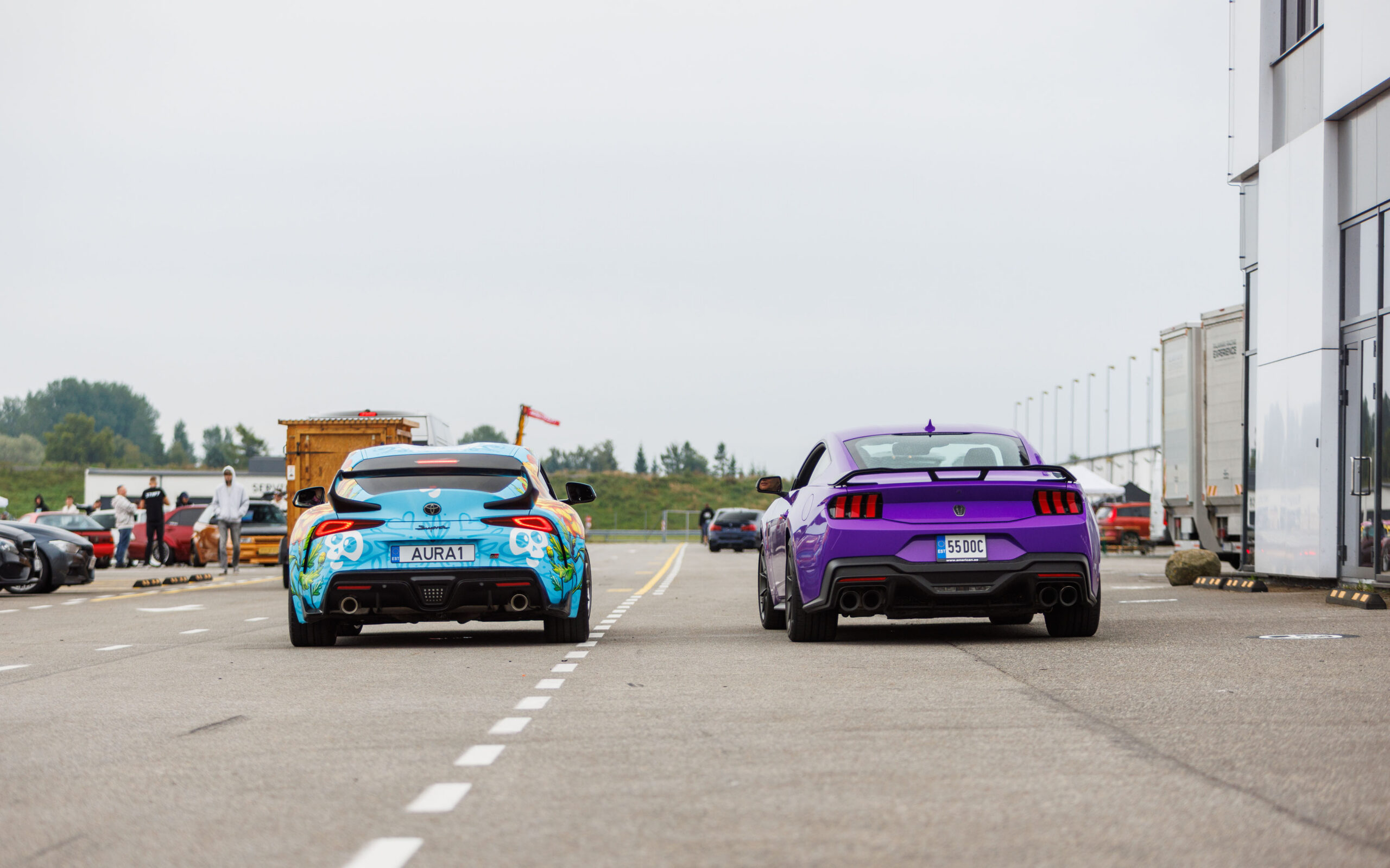 Tagantvaates kirju disainkilega Toyota GR Supra ja lilla Ford Mustang S650 kõrvuti sõitmas Porsche Ringi boksiteel Augustfest 2026 festivalil
