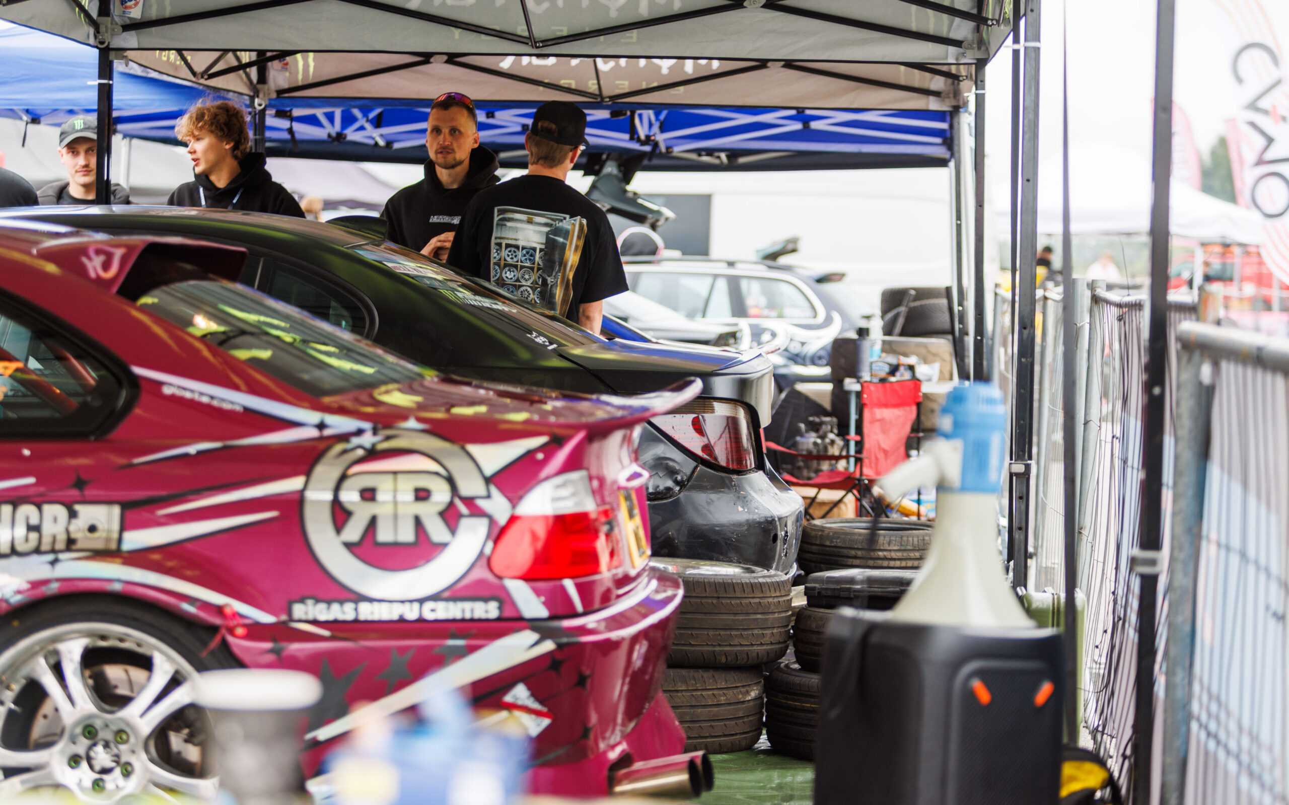 Roosa BMW E46 driftiauto Rigas Riepu Centrs kleebistega ja võistlustiim rehvivirnade vahel telgi all Porsche Ringi paddock-alal Augustfest 2026 festivalil