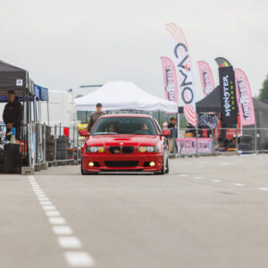 Punane madaldatud BMW E46 sedaan kollaste udutuledega sõitmas Porsche Ringi boksiteel Monster Energy ja telkide vahel Augustfest 2026 festivalil