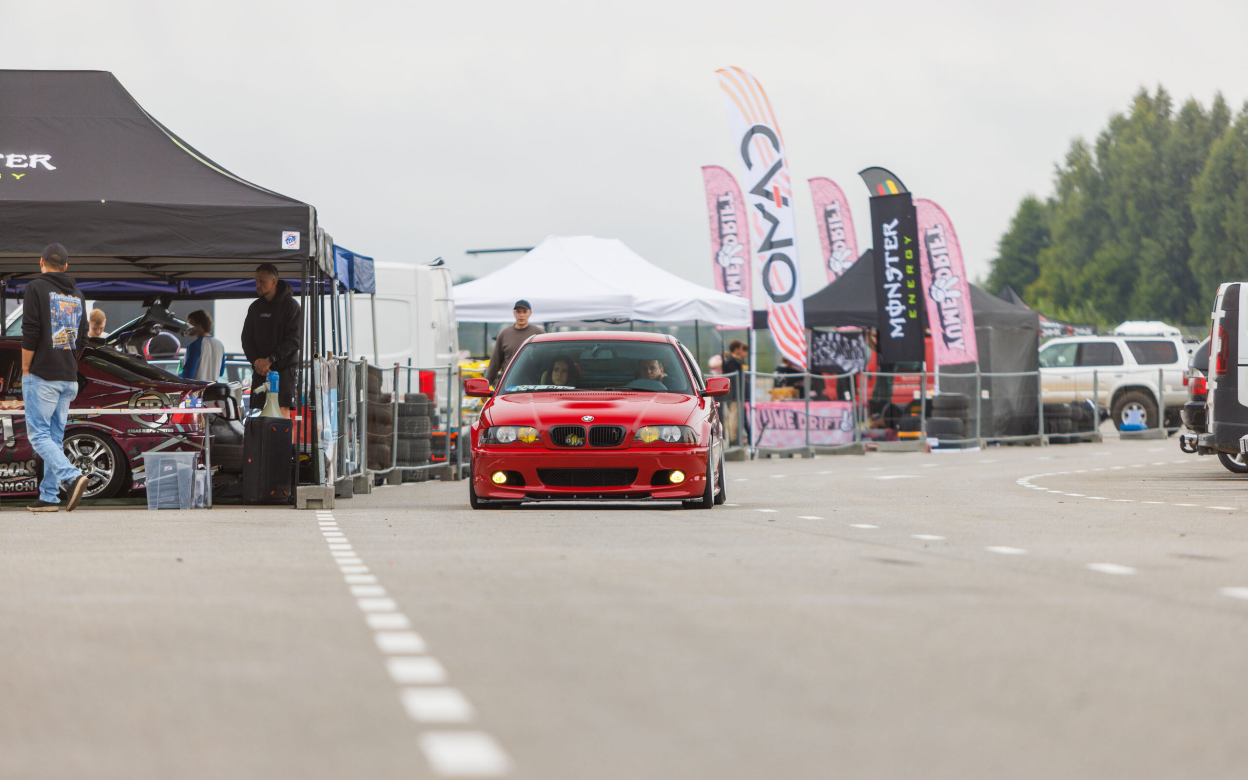 Punane madaldatud BMW E46 sedaan kollaste udutuledega sõitmas Porsche Ringi boksiteel Monster Energy ja telkide vahel Augustfest 2026 festivalil