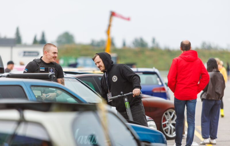 Augustfest korraldustiimi liige tõukerattaga vestlemas turvatöötajaga näituseautode vahel Pärnu Porsche Ringil Augustfest 2026 festivalil