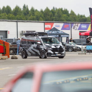 Musta-halli kamoflaažkilega kaetud ja katuseboksiga Volkswagen Transporter T6 buss liikumas Porsche Ringi Drift Taxi ala ees Augustfest 2026 festivalil