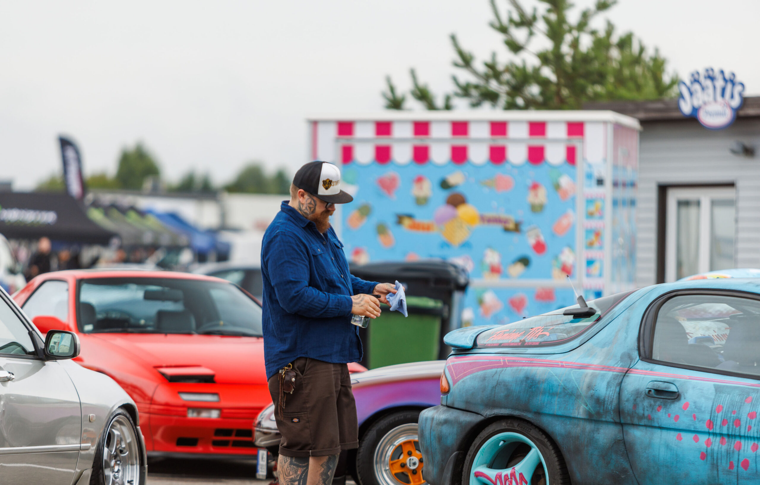 Mees nokamütsis puhastamas lapiga kirjut värvi Mazda MX-3 tuuningautot punase klapptuledega sportauto ees Pärnu Porsche Ringi alal Augustfest 2026 festivalil