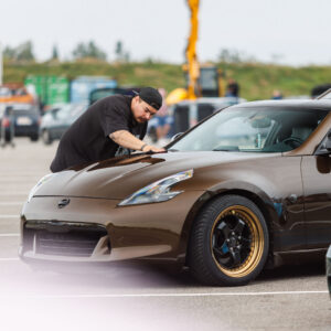 Omanik viimistlemas mikrokiudlapiga pronkspruuni madaldatud Nissan 370Z sportauto kapotti Porsche Ringi näitusealal Augustfest 2026 festivalil