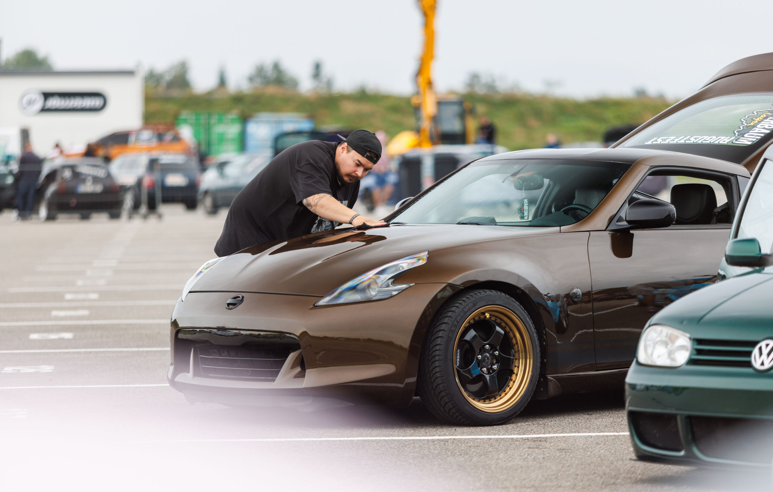 Omanik viimistlemas mikrokiudlapiga pronkspruuni madaldatud Nissan 370Z sportauto kapotti Porsche Ringi näitusealal Augustfest 2026 festivalil