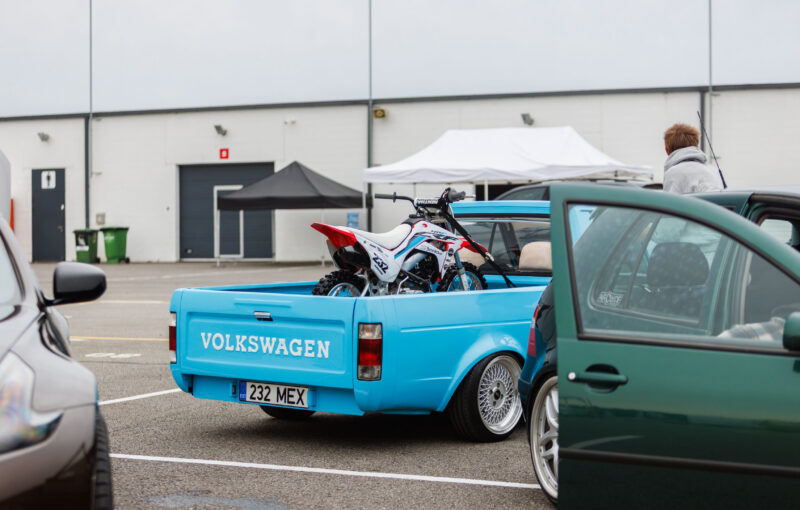 Tagantvaade helesinisest madaldatud Volkswagen Caddy MK1 kastiautost krossimootorrattaga kastis Porsche Ringi boksiteel Augustfest 2026 festivalil