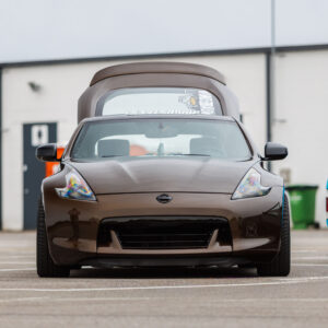 Pronkspruun madaldatud Nissan 370Z sportauto eestvaates avatud tagaluugiga helesinise Volkswagen Caddy kõrval Pärnu Porsche Ringil Augustfest 2026 festivalil