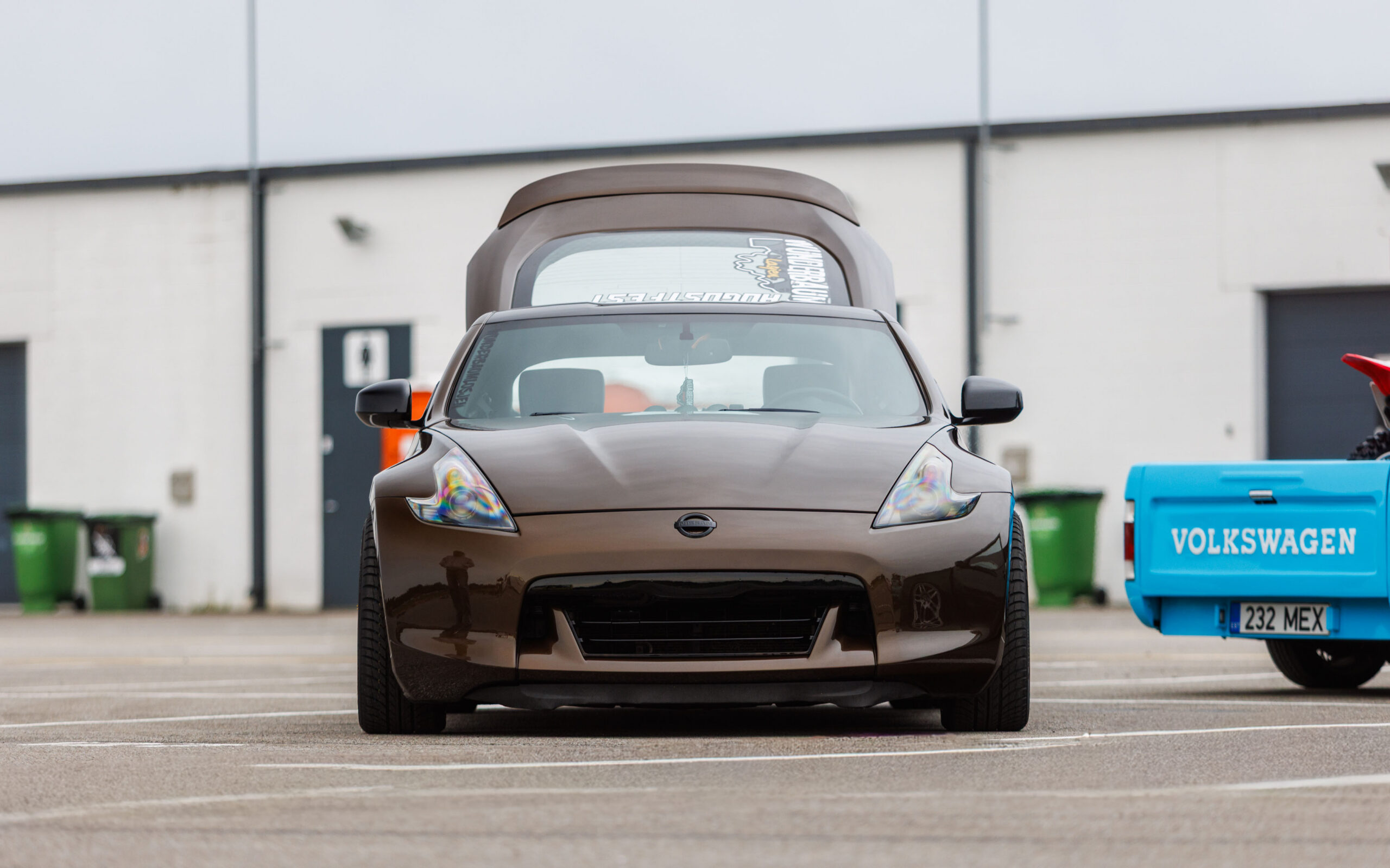 Pronkspruun madaldatud Nissan 370Z sportauto eestvaates avatud tagaluugiga helesinise Volkswagen Caddy kõrval Pärnu Porsche Ringil Augustfest 2026 festivalil