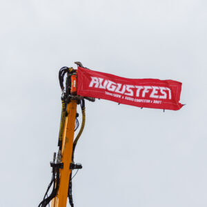 Punane Augustfest bänner kirjadega Tuning Show, Audio Competition ja Drift tõstetud kollase ekskavaatori noole otsa Porsche Ringil Augustfest 2026 festivalil