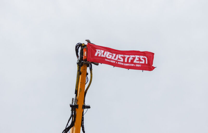 Punane Augustfest bänner kirjadega Tuning Show, Audio Competition ja Drift tõstetud kollase ekskavaatori noole otsa Porsche Ringil Augustfest 2026 festivalil