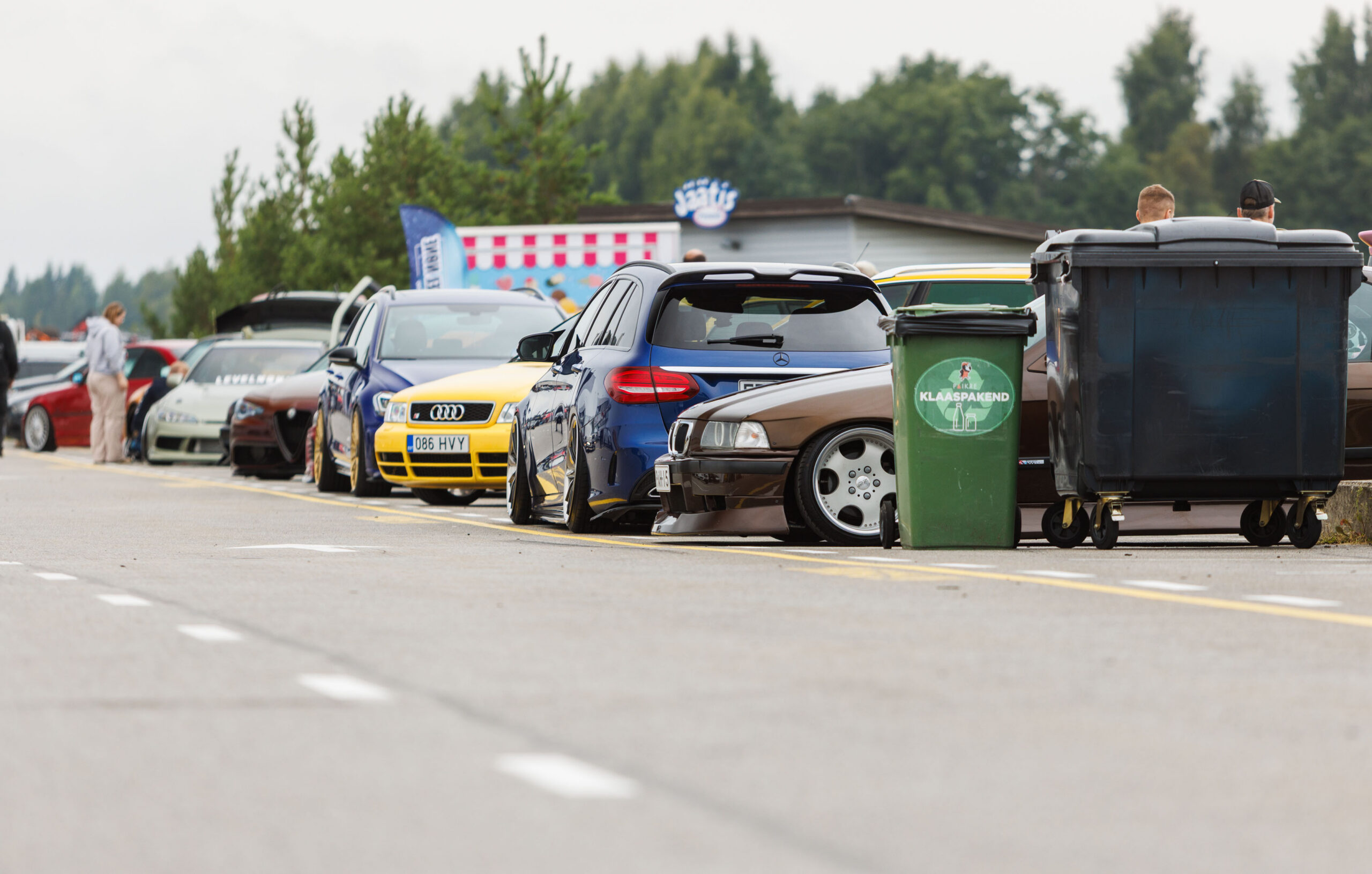 Madaldatud tuuningautode rivi, sealhulgas pruun BMW E36, sinine Mercedes-Benz universaal ja kollane Audi B5 S4 Porsche Ringi näitusealal Augustfest 2026 festivalil