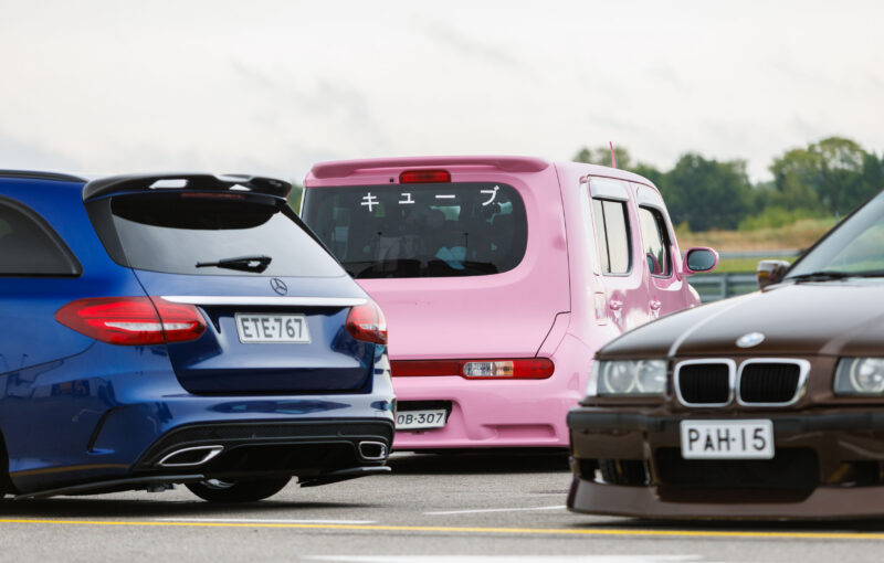 Sinine madaldatud Mercedes-Benzi universaal, roosa Nissan Cube jaapani kirjadega ja pruun BMW E36 seismas Porsche Ringi näitusealal Augustfest 2026 festivalil