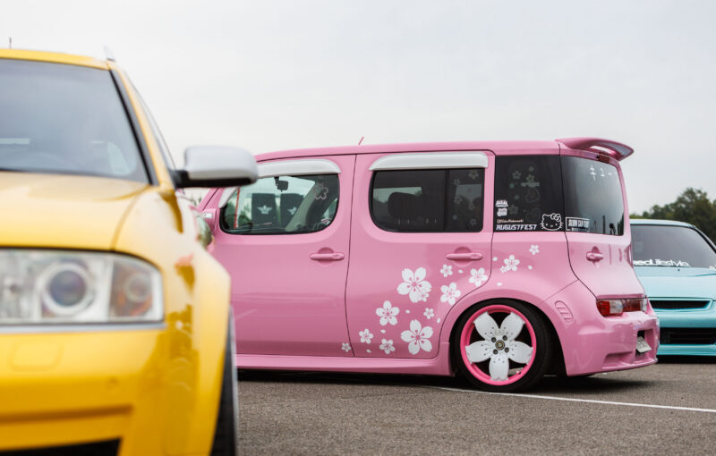 Madaldatud roosa jaapani väikebuss kirsipuu õite graafika, lillekujuliste roosade velgede ja Augustfest kleebisega Porsche Ringil Augustfest 2026 festivalil