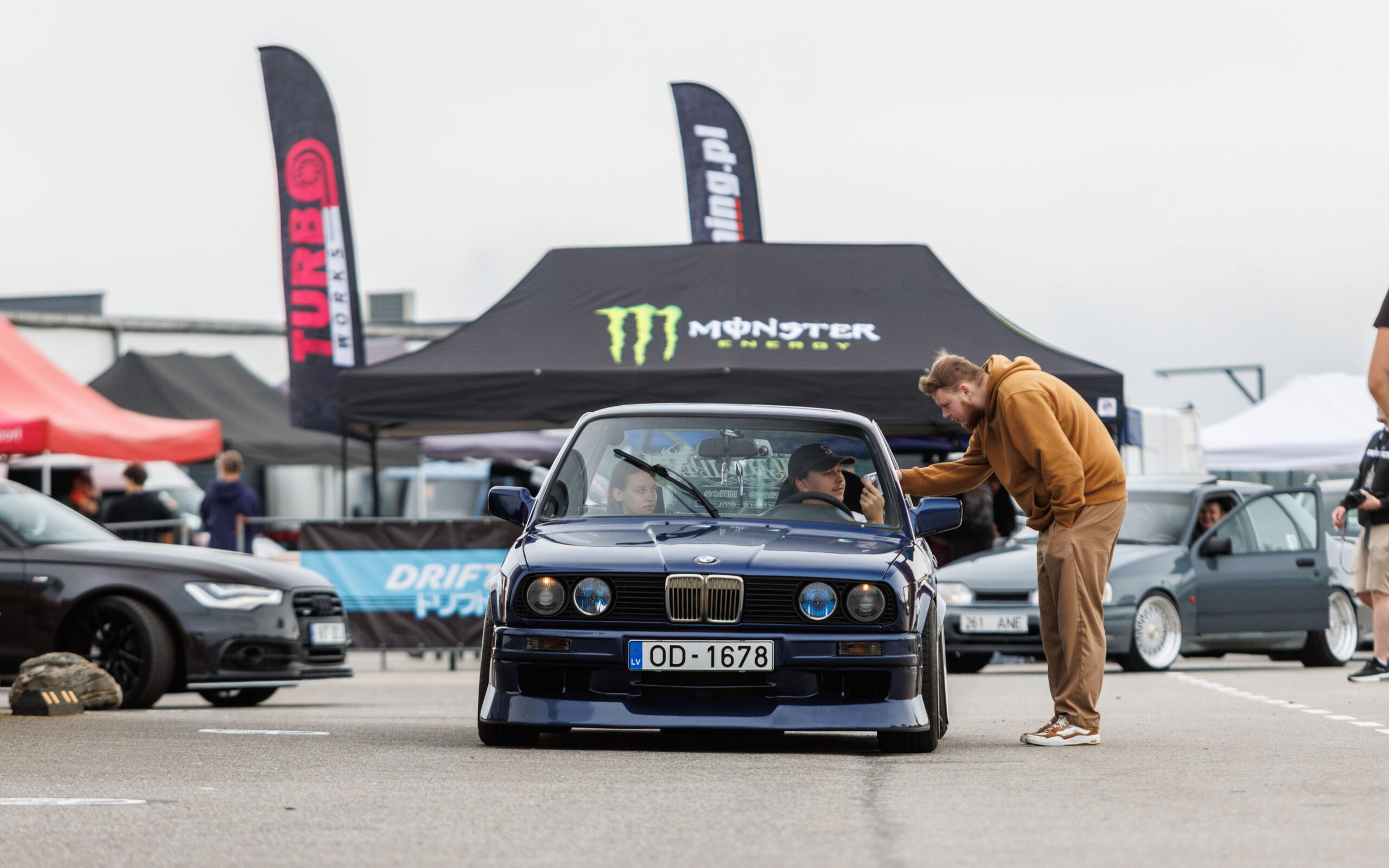 Tumesinine madaldatud BMW E30 sedaan numbrimärgiga OD-1678 seismas boksiteel Monster Energy telgi ees Porsche Ringil Augustfest 2026 festivalil