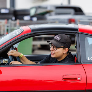 Punase sportauto roolis noormees nokamütsi ja prillidega sõitmas Porsche Ringi boksiteel Augustfest 2026 festivalil Pärnus
