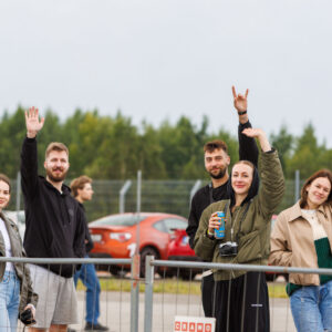Rõõmsad noored pealtvaatajad piirdeaia taga kaamerasse lehvitamas ja käemärke tegemas Pärnu Porsche Ringil Augustfest 2026 festivalil
