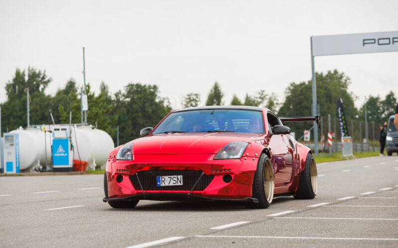 Punane kroomitud laia kerega Nissan 350Z sportauto neetitud tiivalaiendite ja sügava servaga valuvelgedega sõitmas Porsche Ringil Augustfest 2026 festivalil