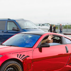 Punane kroomitud widebody Nissan 350Z driftiauto suure tagatiiva ja laiade velgedega, mille juht lehvitab aknast Porsche Ringil Augustfest 2026 festivalil