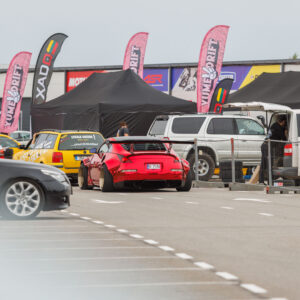 Punane laia kerega Nissan 350Z driftiauto suure tagaspoileri ja kuldsete velgedega sõitmas Porsche Ringi boksiteel Augustfest 2026 festivalil