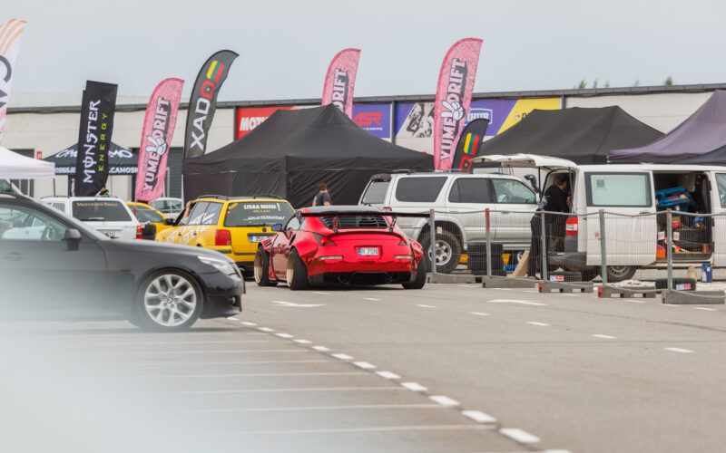 Punane laia kerega Nissan 350Z driftiauto suure tagaspoileri ja kuldsete velgedega sõitmas Porsche Ringi boksiteel Augustfest 2026 festivalil