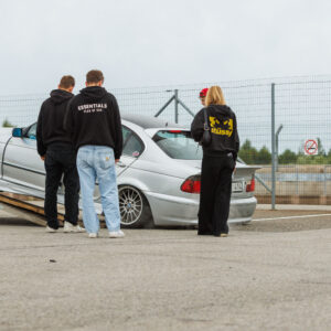Hõbedane madaldatud BMW 3. seeria E46 sedaan mahasõidul autotreilerilt ja noored jälgimas Porsche Ringil Augustfest 2026 festivalil