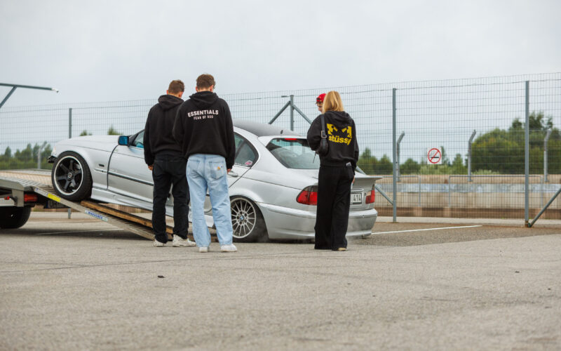 Hõbedane madaldatud BMW 3. seeria E46 sedaan mahasõidul autotreilerilt ja noored jälgimas Porsche Ringil Augustfest 2026 festivalil