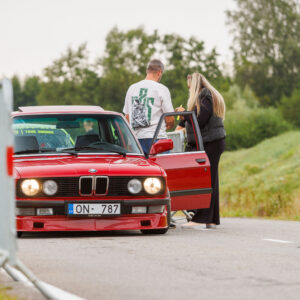 Punane madaldatud BMW E30 sedaan avatud ukse ja põlevate tuledega sissesõiduväravas Pärnu Porsche Ringil Augustfest 2026 festivalil