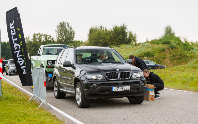 Must maastur BMW X5 E53 vedamas treileril helerohelist Volkswagen Caddy pikapi Monster Energy lipu kõrval Pärnu Porsche Ringil Augustfest 2026 festivalil