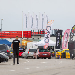 Punane madaldatud BMW E30 sedaan sõitmas Porsche Ringi boksiteel sponsorlippude ja Porsche lipumastide vahel Augustfest 2026 festivalil Pärnus