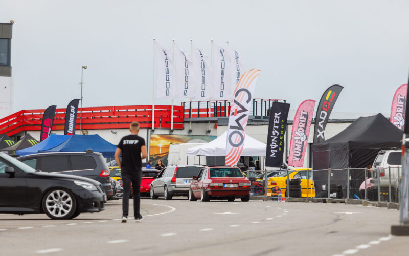Punane madaldatud BMW E30 sedaan sõitmas Porsche Ringi boksiteel sponsorlippude ja Porsche lipumastide vahel Augustfest 2026 festivalil Pärnus