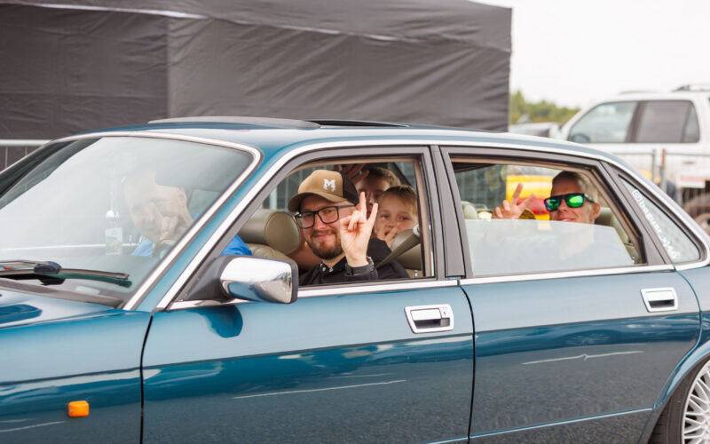 Rõõmsad inimesed sinakasrohelises klassikalises Jaguar XJ40 sedaanis käemärke näitamas Pärnu Porsche Ringil Augustfest 2026 festivalil