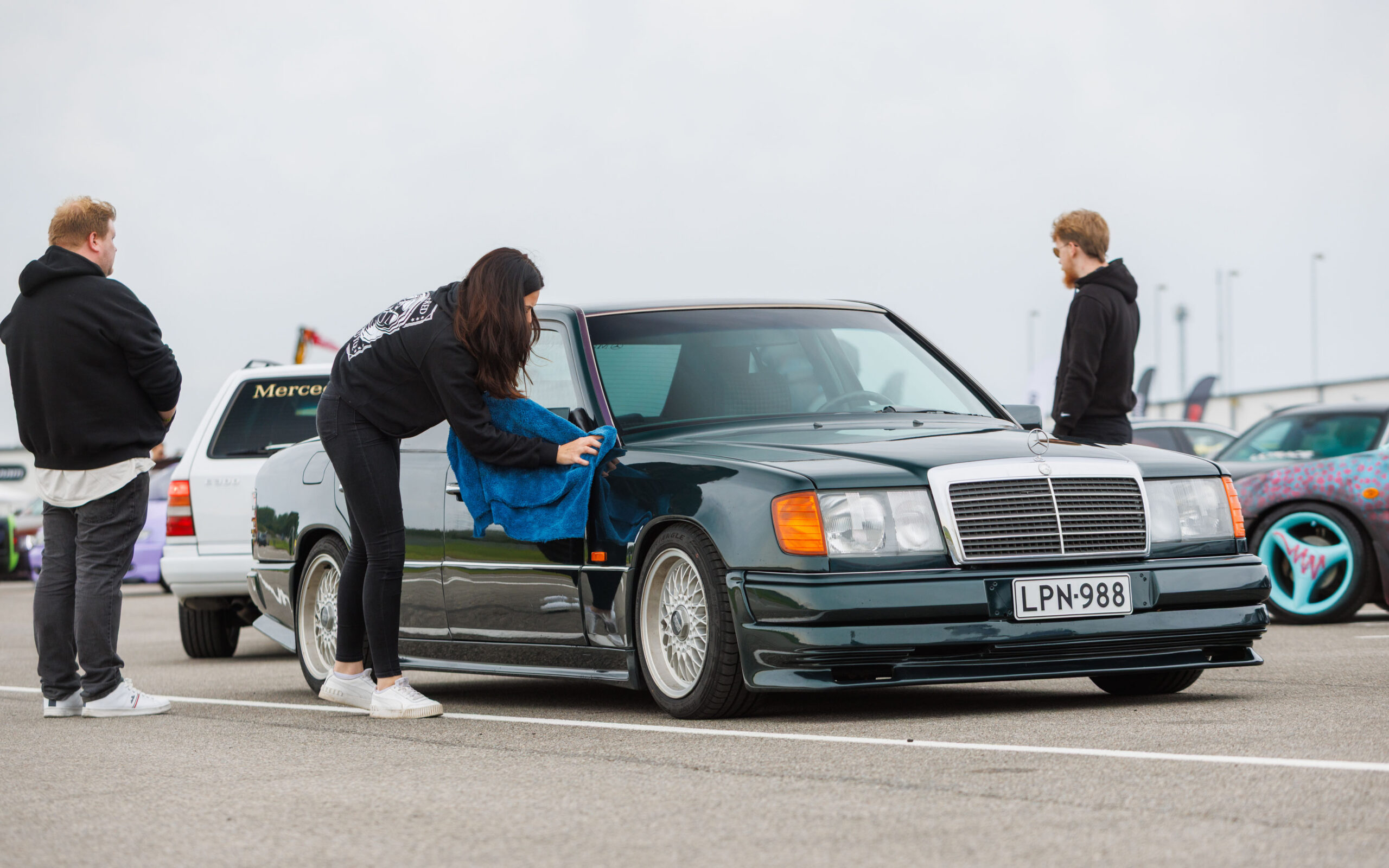 Tumesinine klassikaline madaldatud Mercedes-Benz W124 sedaan kärgvelgedega, mida naine mikrokiudlapiga puhastab Pärnu Porsche Ringil Augustfest 2026 festivalil