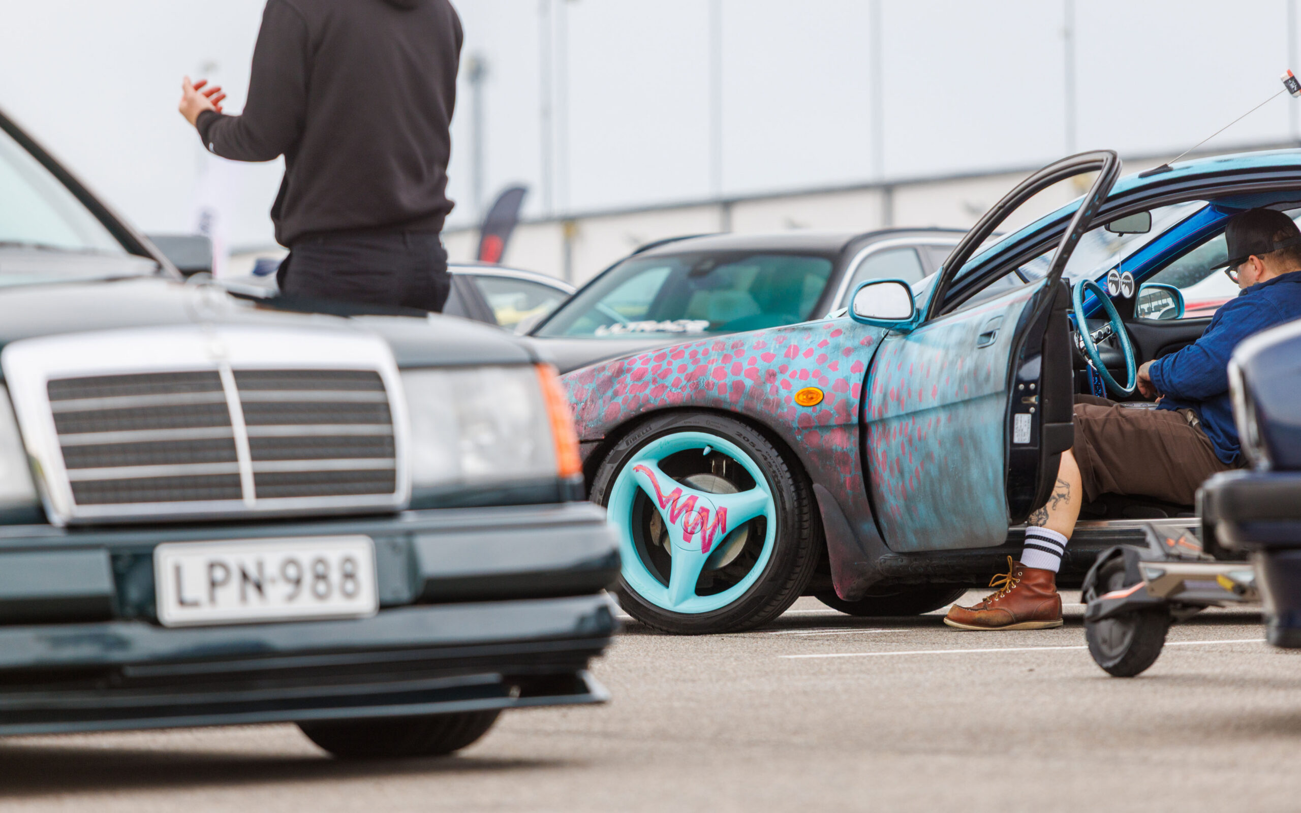 Kirju kohandatud värvkatte ja helesiniste kolme kodaraga velgedega tuuningauto tumeda klassikalise Mercedes-Benzi kõrval Pärnu Porsche Ringil Augustfest 2026 festivalil