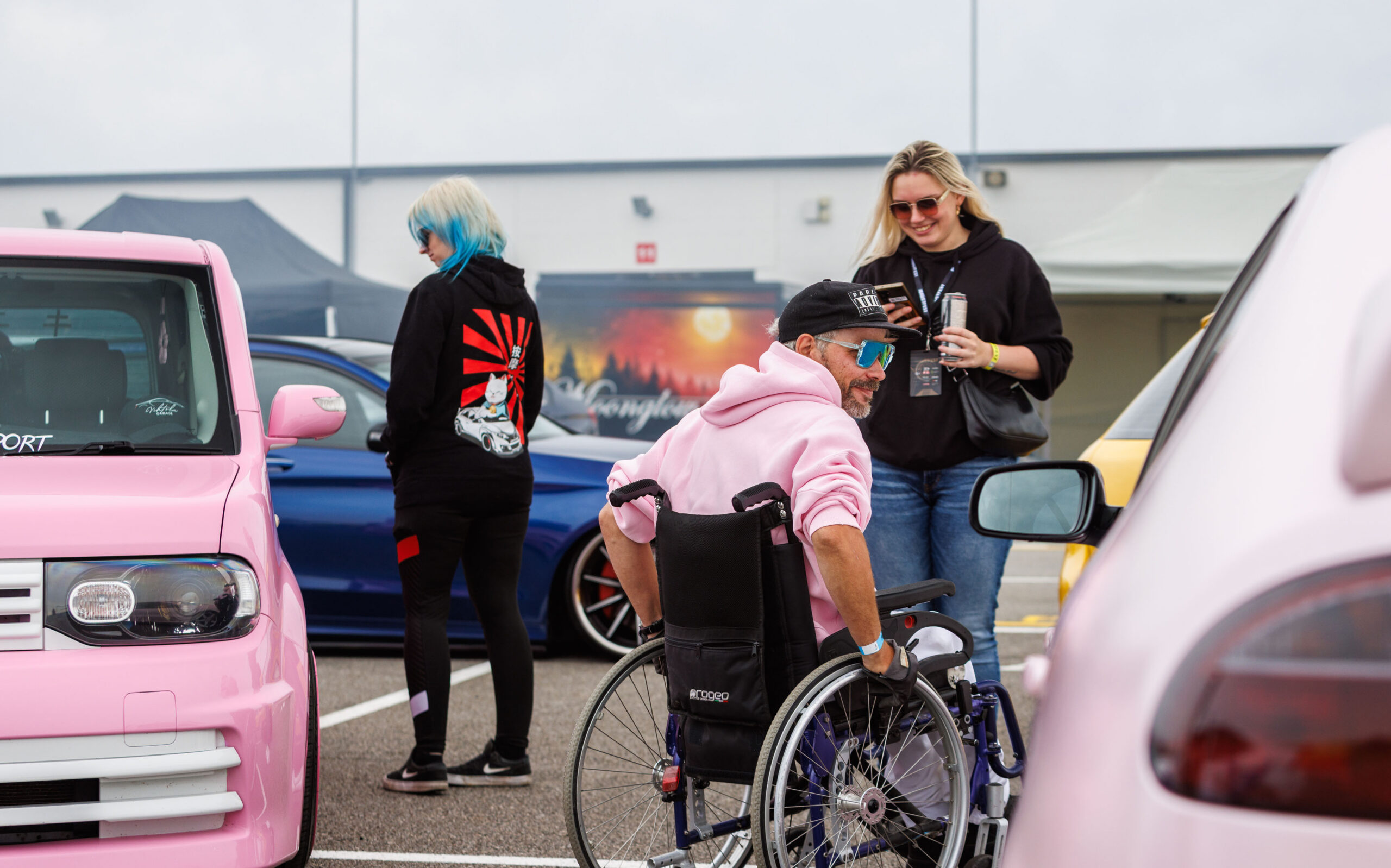 Ratastoolis mees ja külastajad seismas heleroosa tuunitud Jaapani Kei-car auto kõrval Pärnu Porsche Ringil Augustfest 2026 festivalil