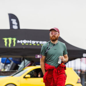Punases võidusõidukombinesoonis ja päikeseprillidega mees kõndimas Monster Energy telgi ja kollase auto ees Pärnu Porsche Ringil Augustfest 2026 festivalil