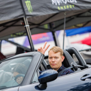 Naeratav noormees lahtise Mazda MX-5 kabrioleti roolis näitamas rahumärki Pärnu Porsche Ringil Augustfest 2026 festivalil