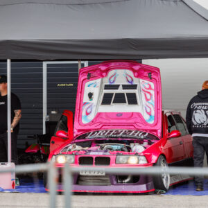 Erkroosa BMW E36 driftiauto avatud leegimustriga kapotiga ja Drift HQ kirjaga boksi telgi all Pärnu Porsche Ringil Augustfest 2026 festivalil