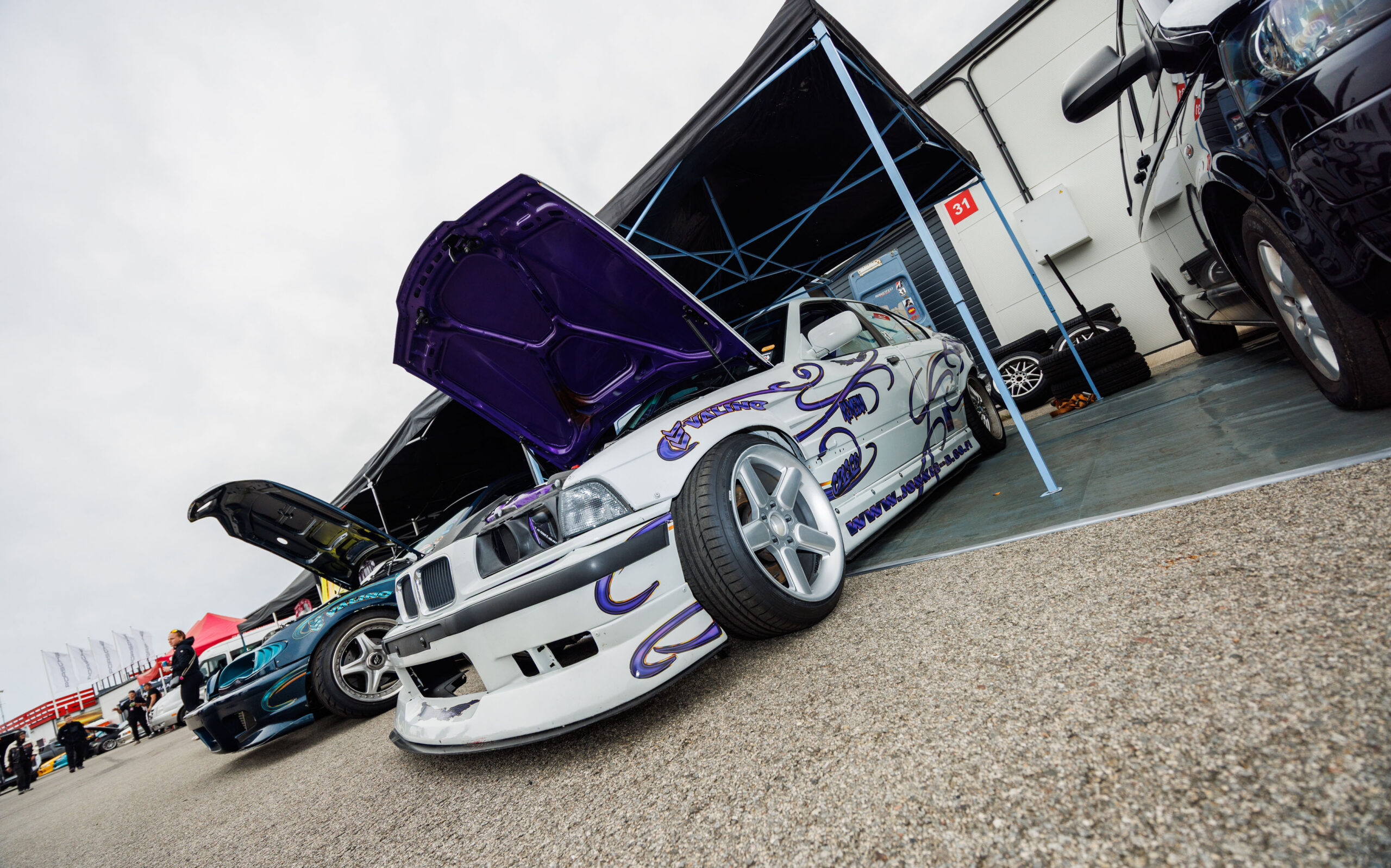 Valge BMW E36 driftiauto lillade leekide ja avatud lilla kapotialusega boksis Pärnu Porsche Ringil Augustfest 2026 festivalil